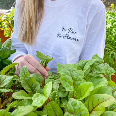 woman wearing white long sleeve shirt that says "No Rain No Flowers"